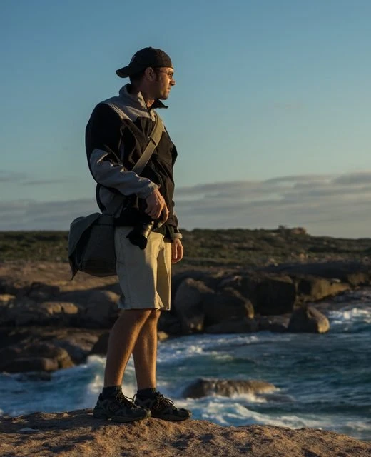 Jacob Maentz with his camera bag on a coastal headland, cropped closer from the original photograph.